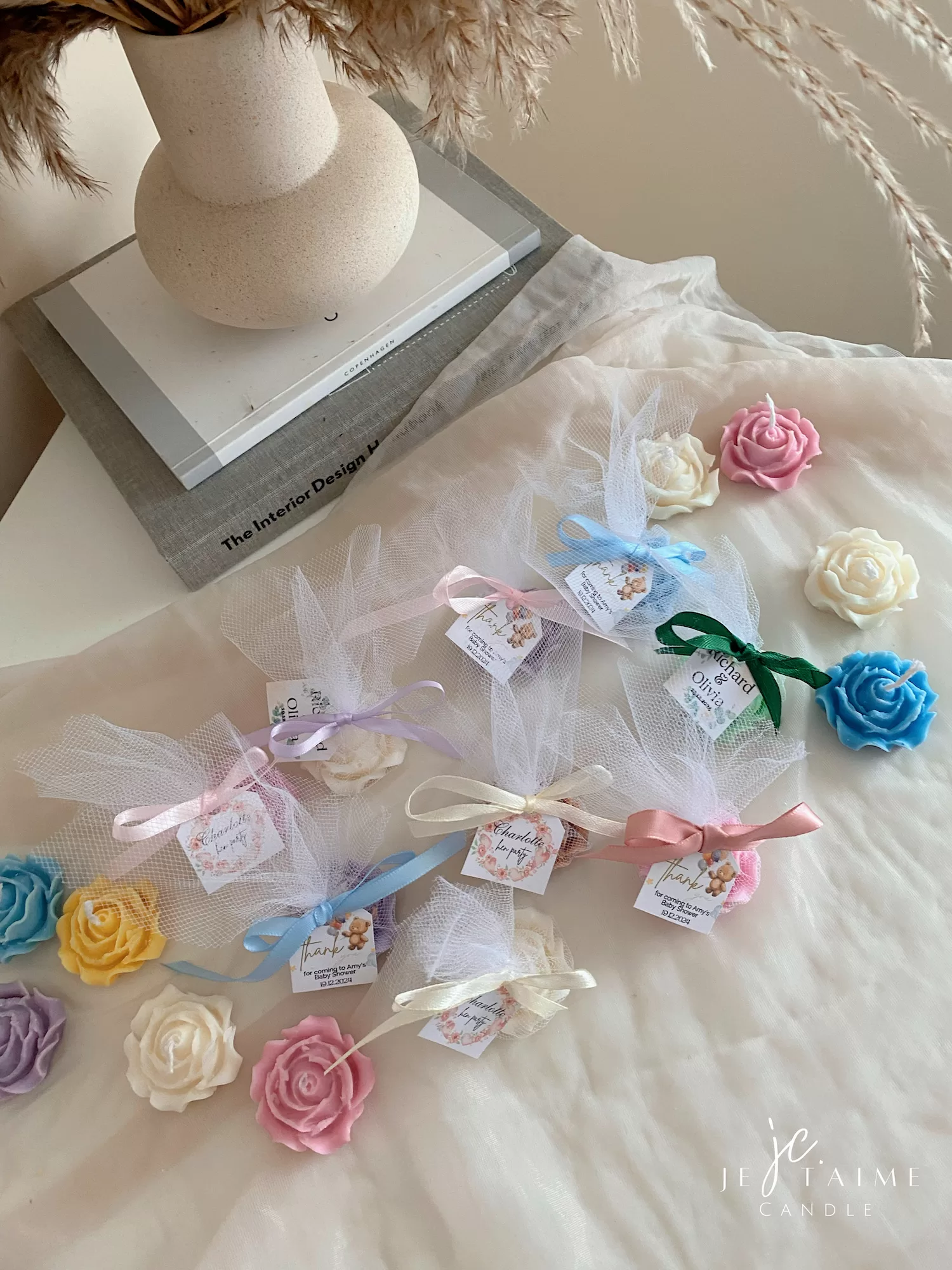 Colorful rose candles in pink, blue, yellow, and white, wrapped in white organza bags with personalized 'Thank You' tags for Amy's baby shower on 12/01/2024, displayed with pampas grass decor in the background