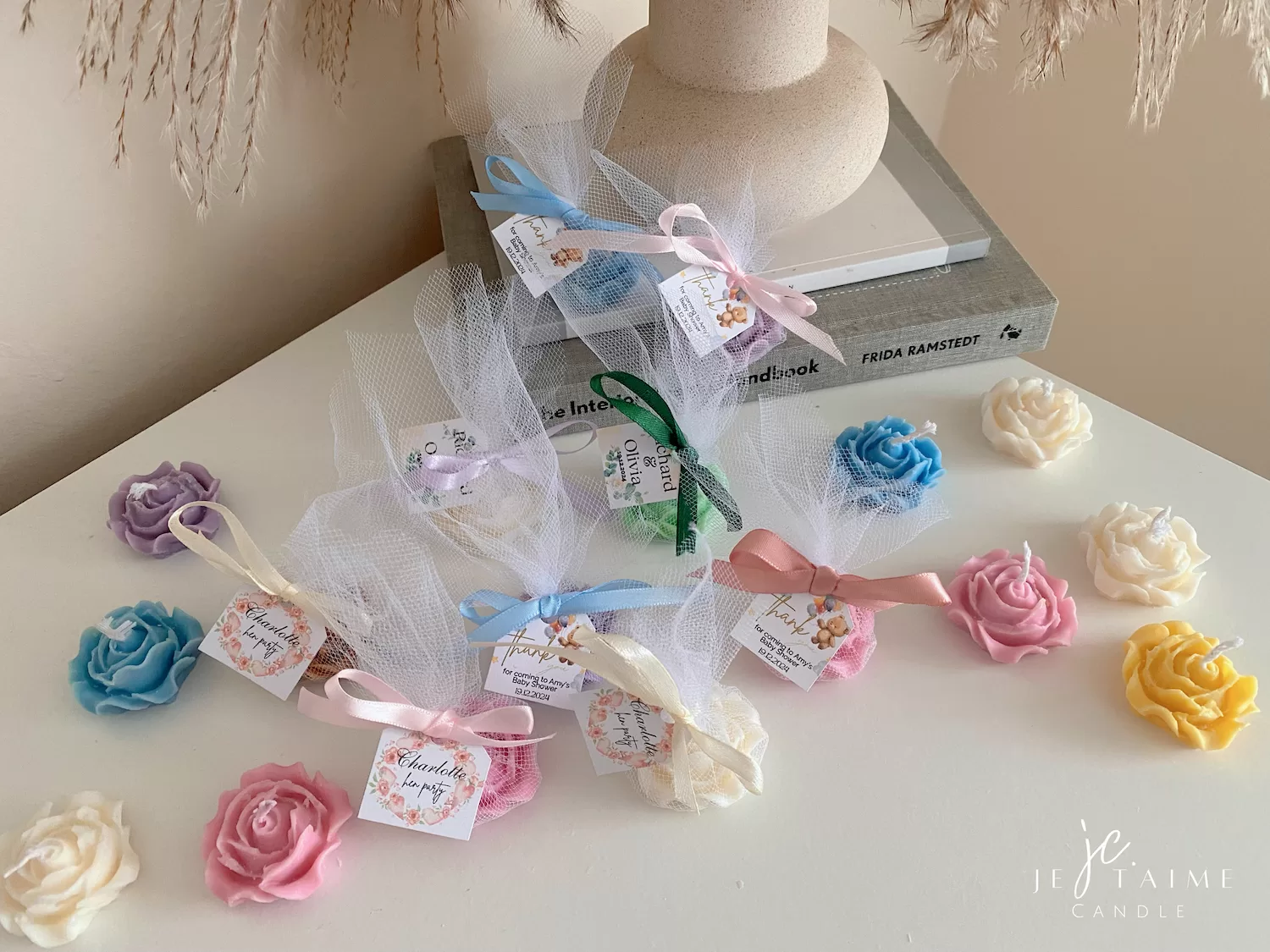 Colorful rose candles in pink, blue, yellow, and white, wrapped in white organza bags with personalized 'Thank You' tags for Amy's baby shower on 12/01/2024, displayed with pampas grass decor in the background