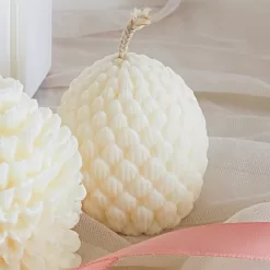 Pine cone-shaped candles displayed, set on soft fabric with a pink ribbon accent.