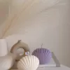 Two seashell-shaped candles in pastel tones, one lavender purple and one ivory white, displayed on a wooden tray with matches beside them. These handmade soy wax seashell candles feature a ribbed shell design, perfect as coastal home décor, beach wedding decorations, summer party favors, or unique handmade gifts. Minimalist and aesthetic, these shell candles bring a serene seaside vibe to any room.
