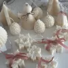 A collection of decorative candles in various shapes, including snowflakes, a Christmas tree, a nutcracker, a house, and a cylindrical candle. The snowflake candles are intricately designed in white, displayed on soft fabric.