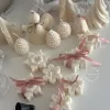 A collection of decorative candles in various shapes, including snowflakes, a Christmas tree, a nutcracker, a house, and a cylindrical candle. The snowflake candles are intricately designed in white, displayed on soft fabric.