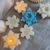 A collection of decorative candles in various shapes, including snowflakes, a Christmas tree, a nutcracker, a house, and a cylindrical candle. The snowflake candles are intricately designed in white and blue, displayed on soft fabric.
