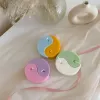 Four pastel yin-yang shaped candles in pairs of pink and purple, yellow and blue, green and cream, displayed on a white surface with a pink polka-dotted felt ball, a butter-themed box, and a disco ball nearby.