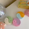 Four pastel yin-yang shaped candles in pairs of pink and purple, yellow and blue, green and cream, displayed on a white surface with a pink polka-dotted felt ball, a butter-themed box, and a disco ball nearby.