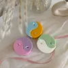 Four pastel yin-yang shaped candles in pairs of pink and purple, yellow and blue, green and cream, displayed on a white surface with a pink polka-dotted felt ball, a butter-themed box, and a disco ball nearby.