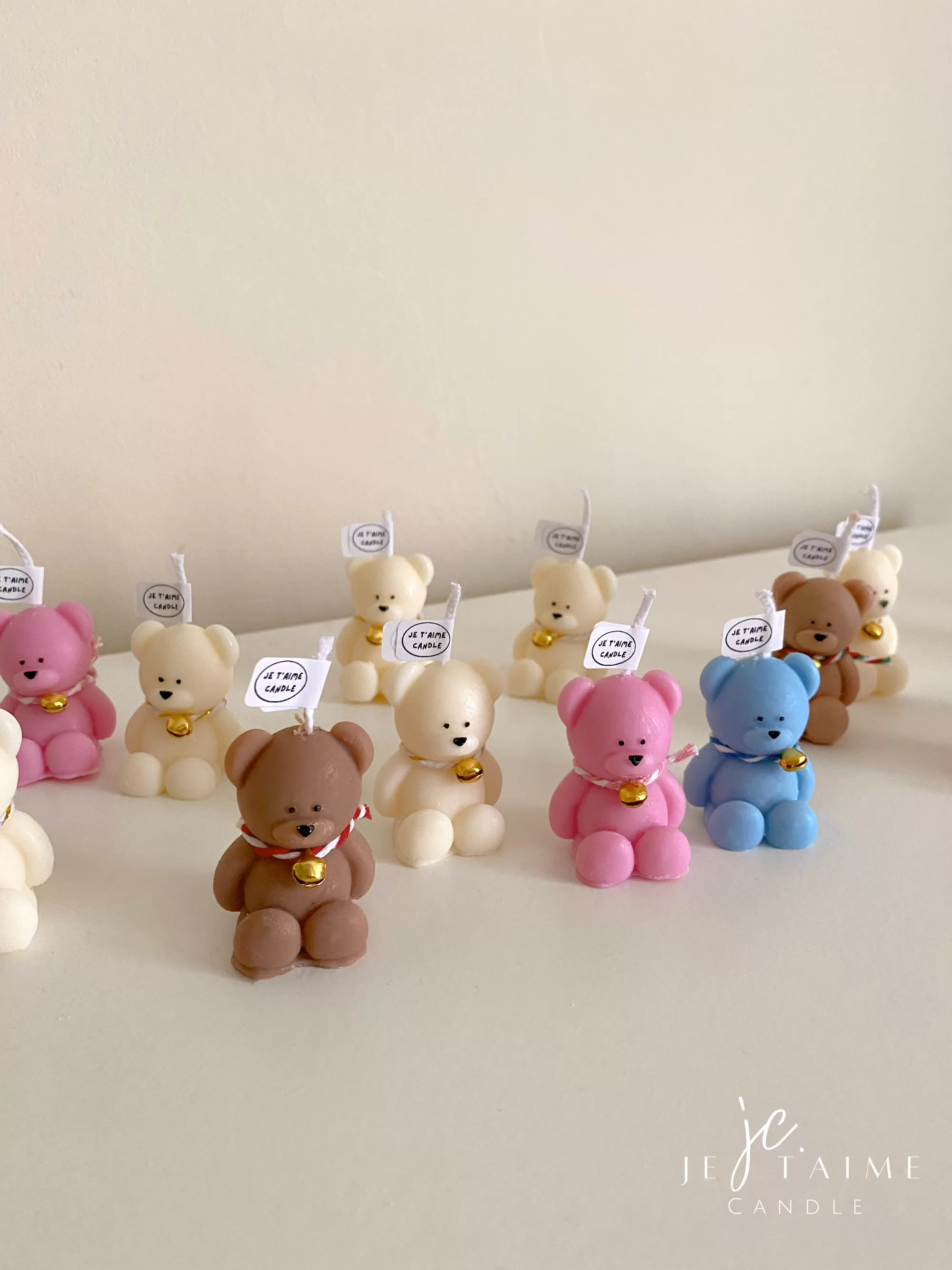 Adorable mini teddy bear candles in cream, pink, blue and brown with gold bell charms, displayed on a white table. Perfect baby shower favors, gender reveal party gifts, or cute keepsakes for guests.