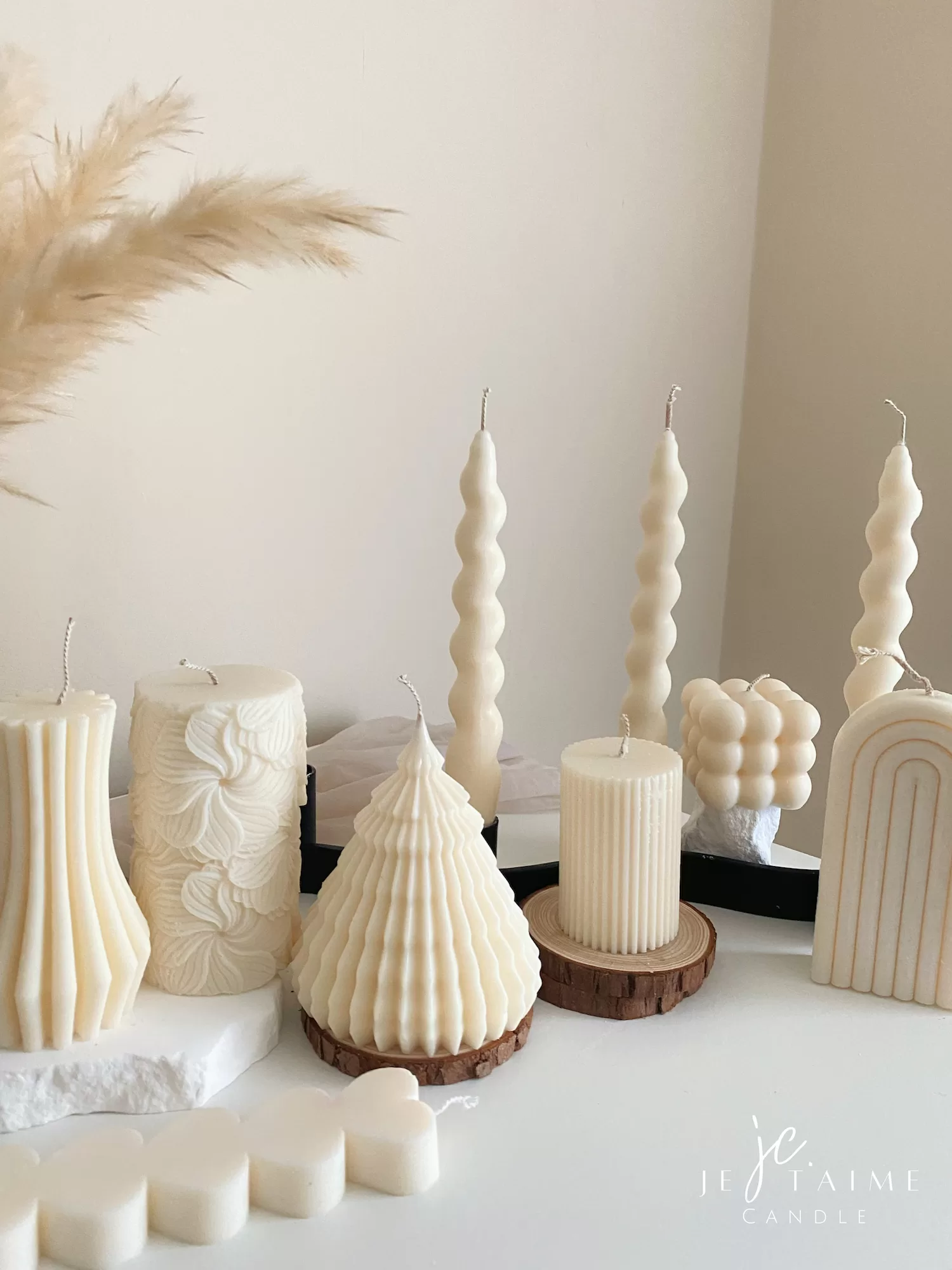 Handmade aesthetic candle in ivory soy wax with a modern fluted design, displayed on a white stone base with pampas grass and other decorative candles in the background. This sculptural column candle is perfect for minimalist home décor, wedding centerpieces, or as a unique handmade gift, adding timeless elegance and modern style to any space.