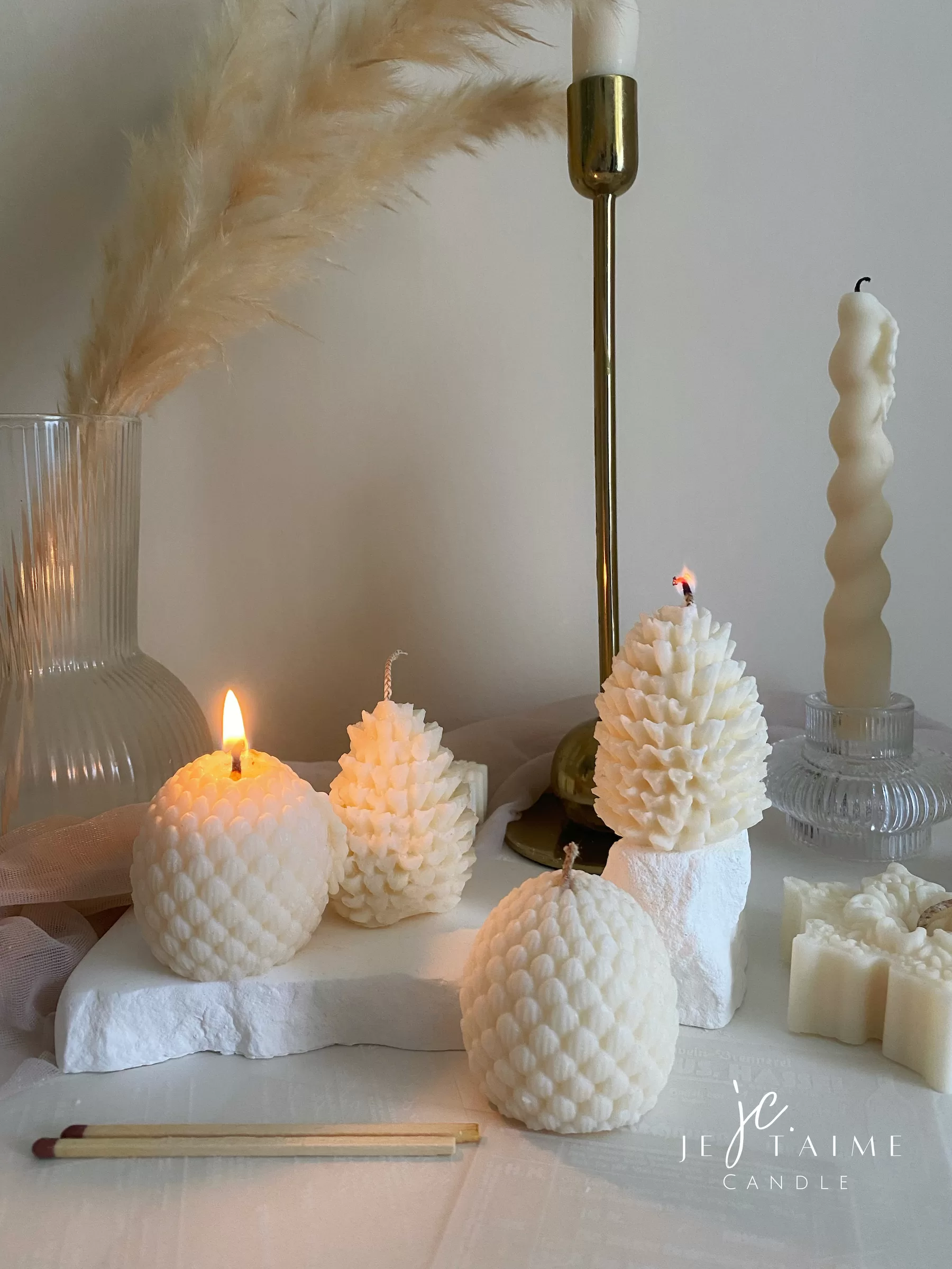 Assorted handmade Christmas candles in festive shapes including Pinecone, snowflakes, taper candle, displayed together in holiday-themed colors.