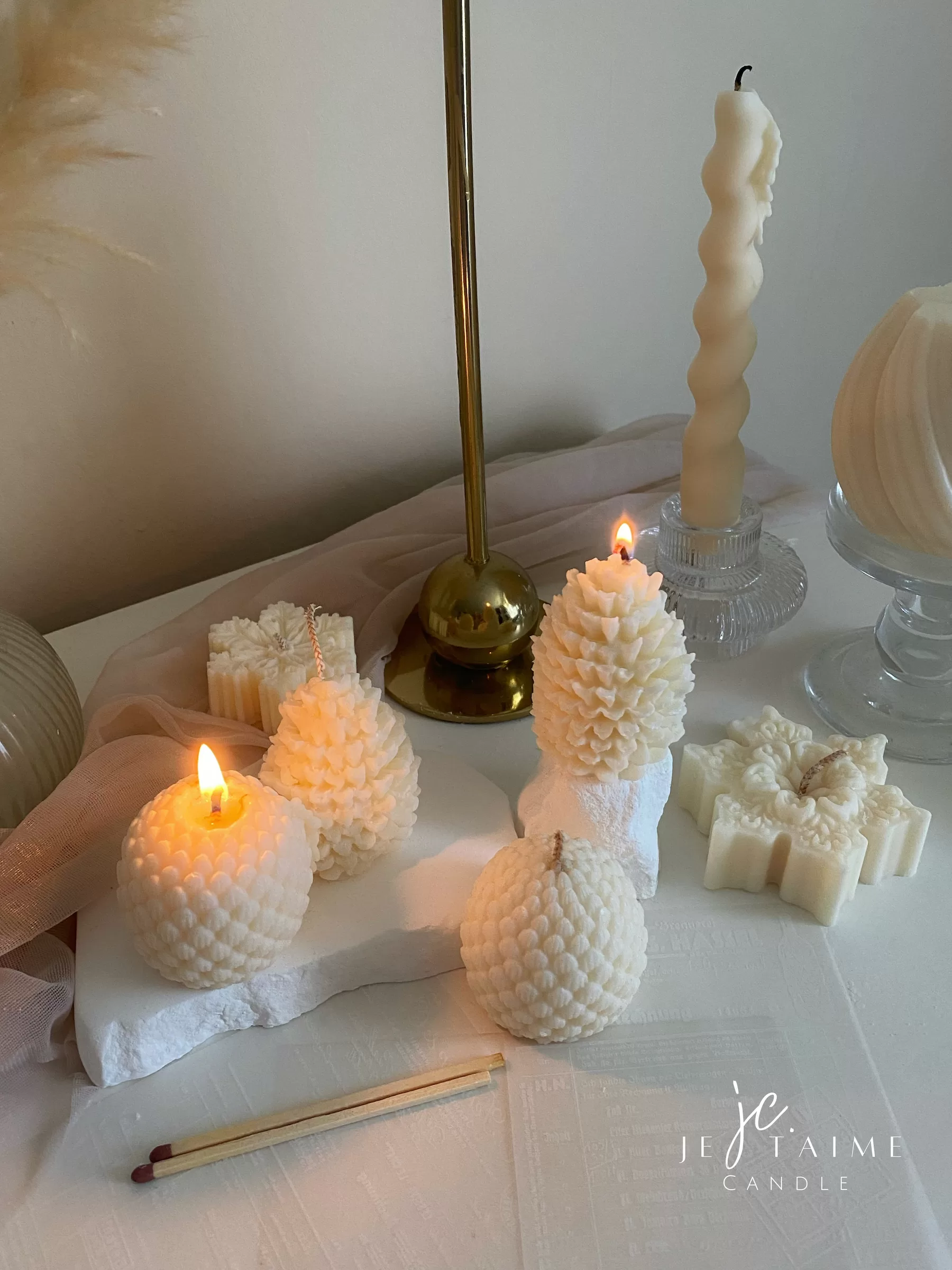 Assorted handmade Christmas candles in festive shapes including Pinecone, snowflakes, taper candle, displayed together in holiday-themed colors.