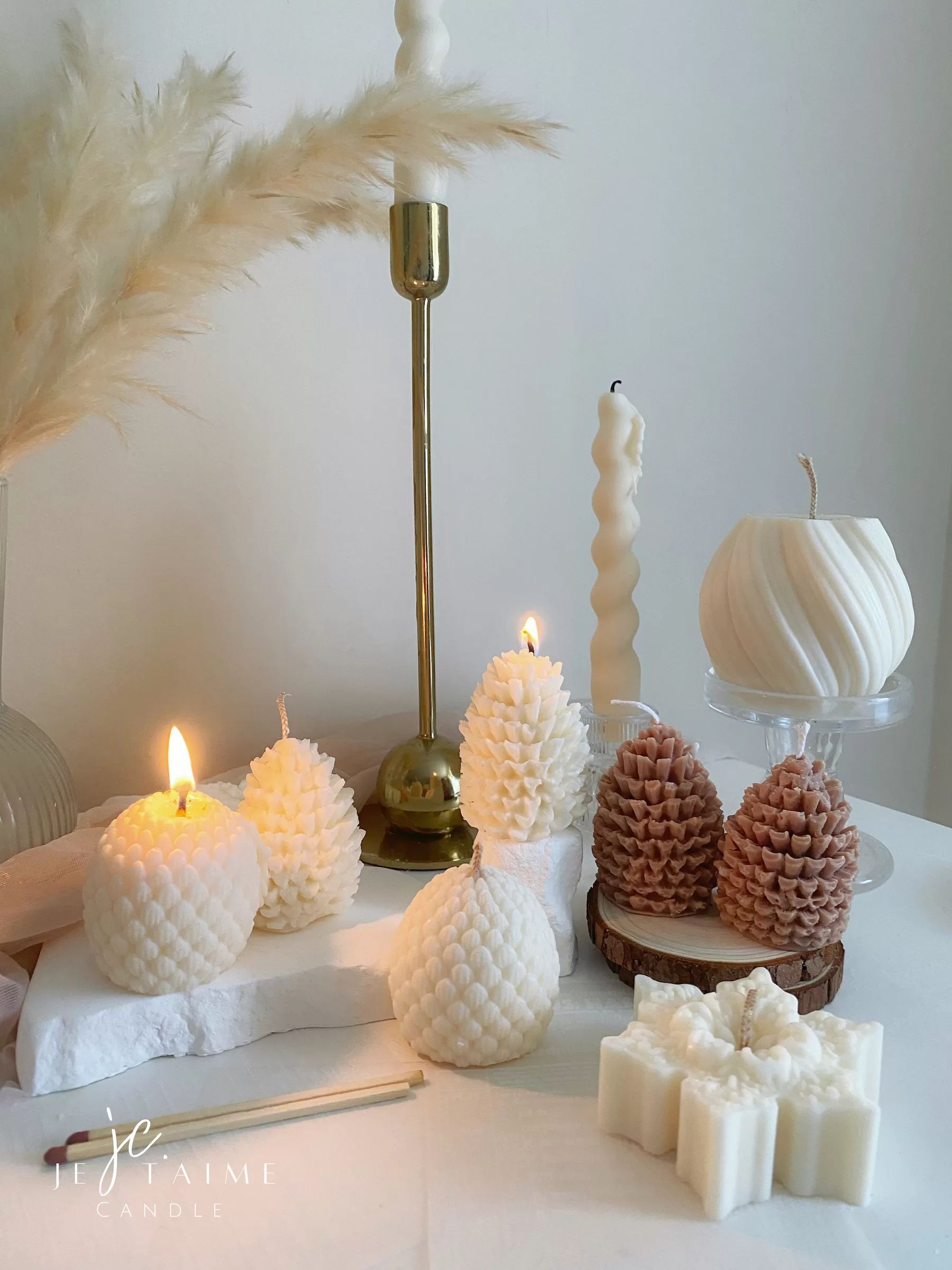 Assorted handmade Christmas candles in festive shapes including Pinecone, snowflakes, taper candle, displayed together in holiday-themed colors.
