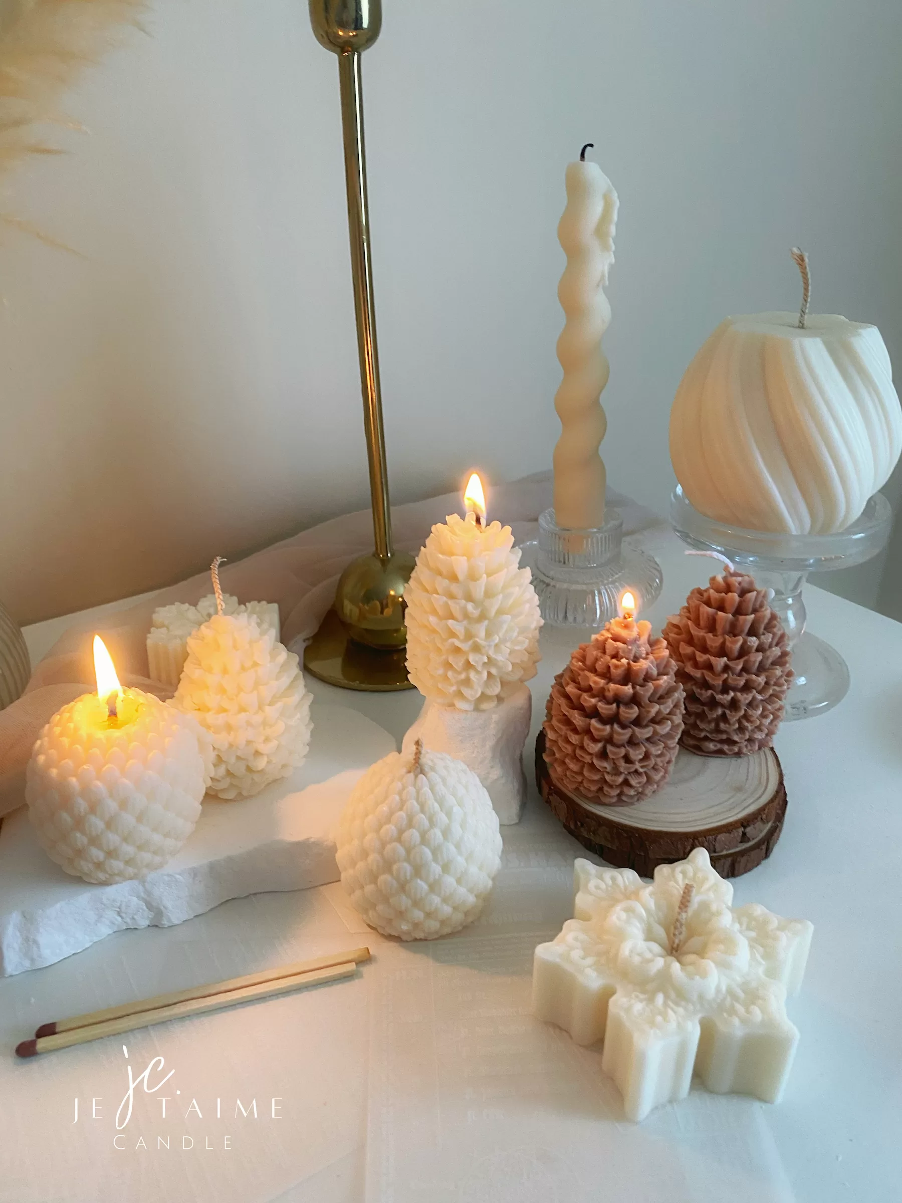 Assorted handmade Christmas candles in festive shapes including Pinecone, snowflakes, taper candle, displayed together in holiday-themed colors.