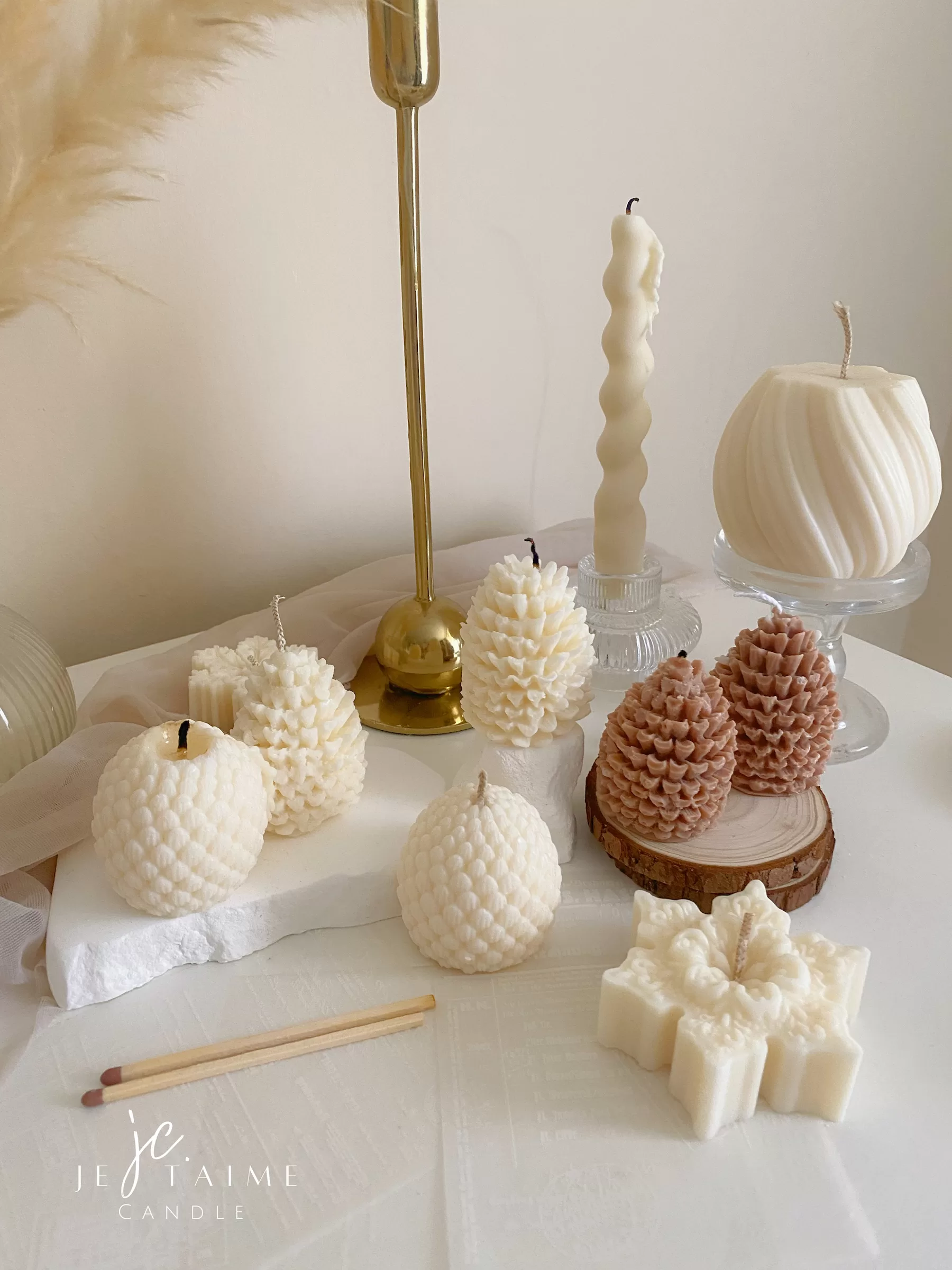Assorted handmade Christmas candles in festive shapes including Pinecone, snowflakes, taper candle, displayed together in holiday-themed colors.