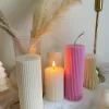 Two handmade ribbed pillar candles in ivory white and pink soy wax, one tall and one short, placed on a white stone base beside pampas grass, a gold candle holder, and decorative candles. The ribbed texture gives these candles a modern minimalist look, making them ideal for wedding centerpieces, cozy home décor, or as stylish handmade gifts. Their clean design and neutral color make them versatile decorative accents that fit perfectly into Scandinavian, modern, and rustic interiors.