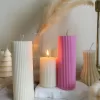 Two handmade ribbed pillar candles in ivory white and pink soy wax, one tall and one short, placed on a white stone base beside pampas grass, a gold candle holder, and decorative candles. The ribbed texture gives these candles a modern minimalist look, making them ideal for wedding centerpieces, cozy home décor, or as stylish handmade gifts. Their clean design and neutral color make them versatile decorative accents that fit perfectly into Scandinavian, modern, and rustic interiors.