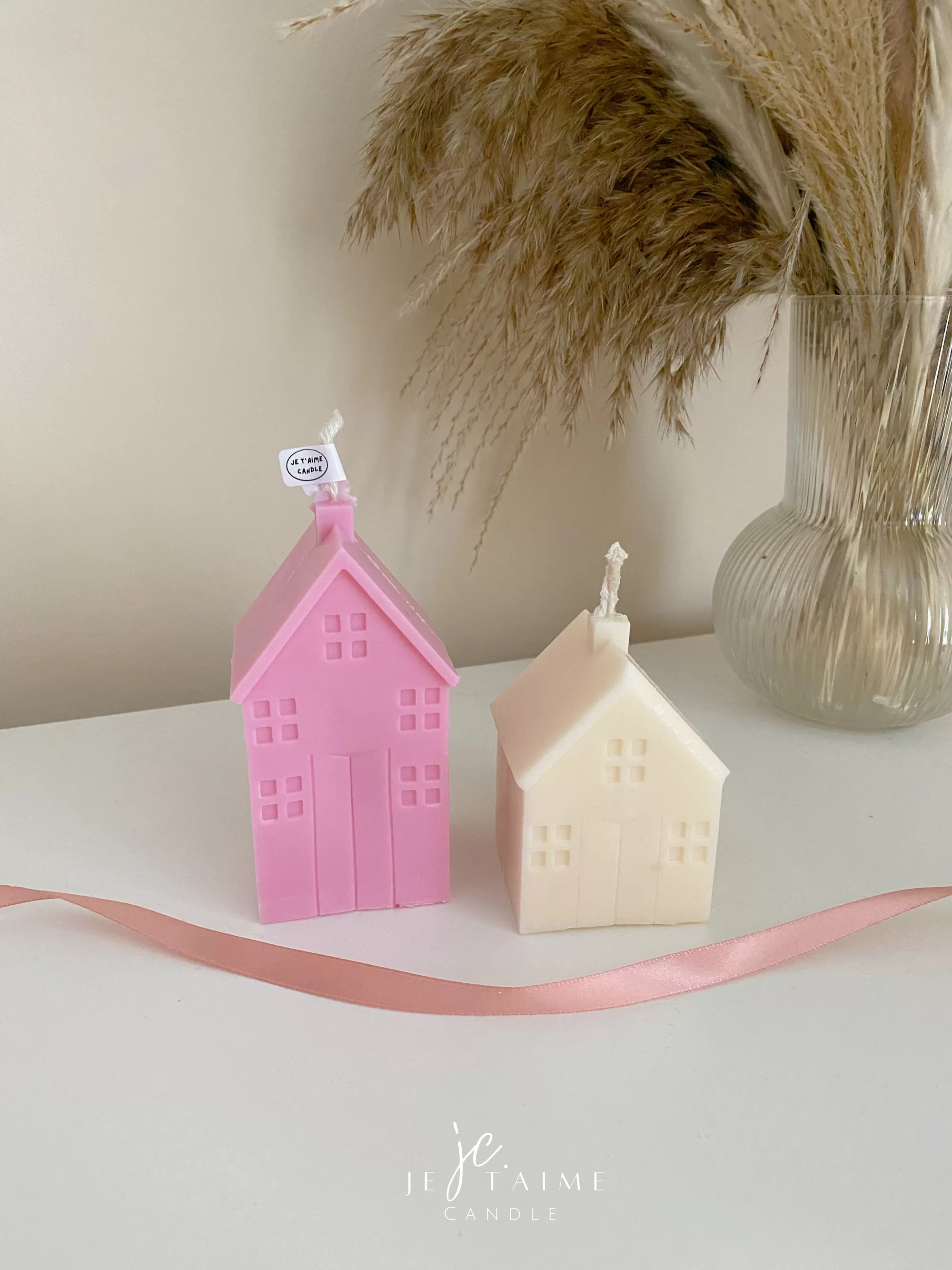 Two pink house-shaped candles on a table, perfect for housewarming gifts and cozy home decor.