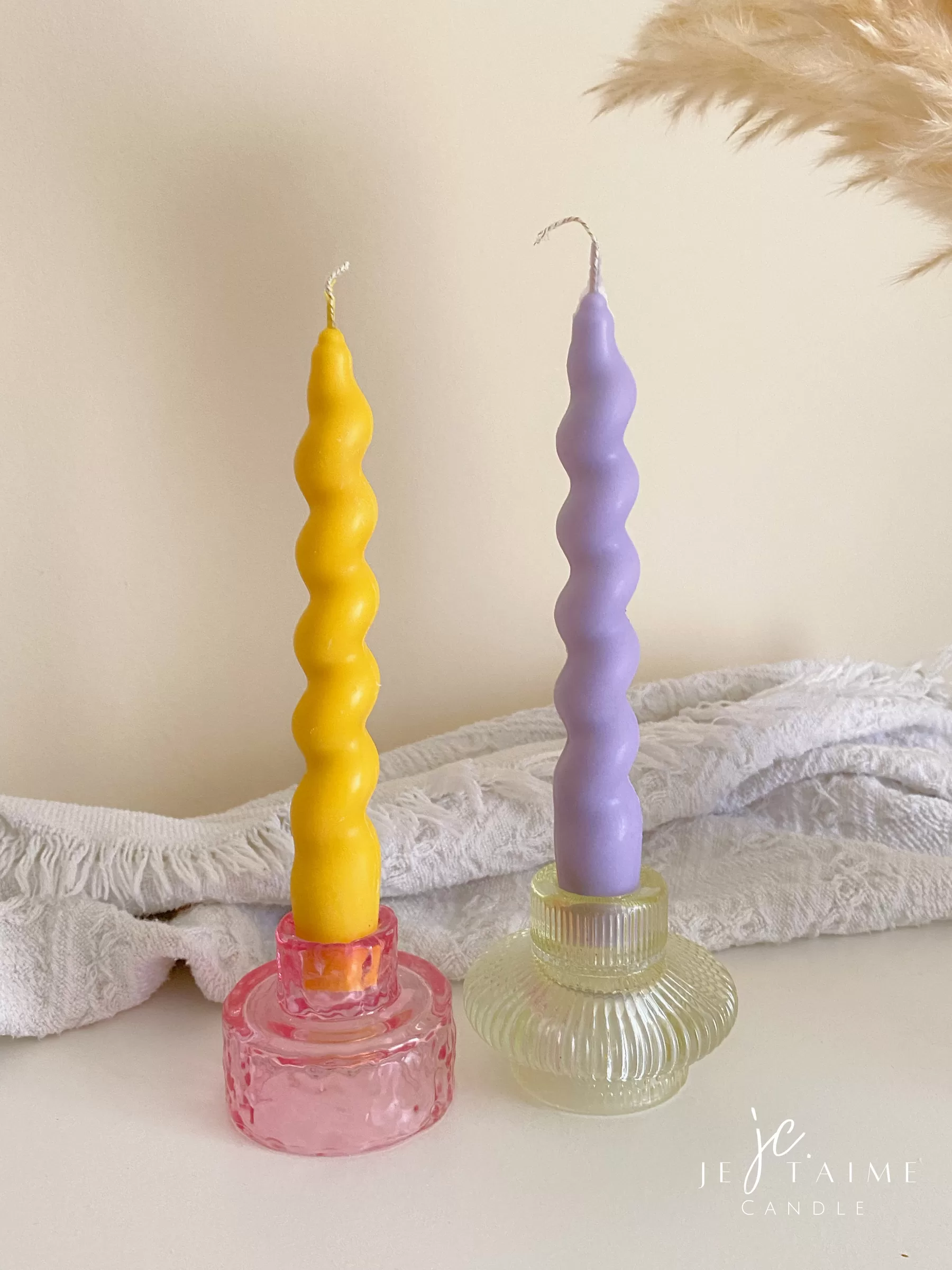 Set of colorful spiral twist soy wax taper candles in pastel yellow and purple, displayed in clear glass holders, perfect for dinner table decor, wedding centerpieces, and modern home styling.