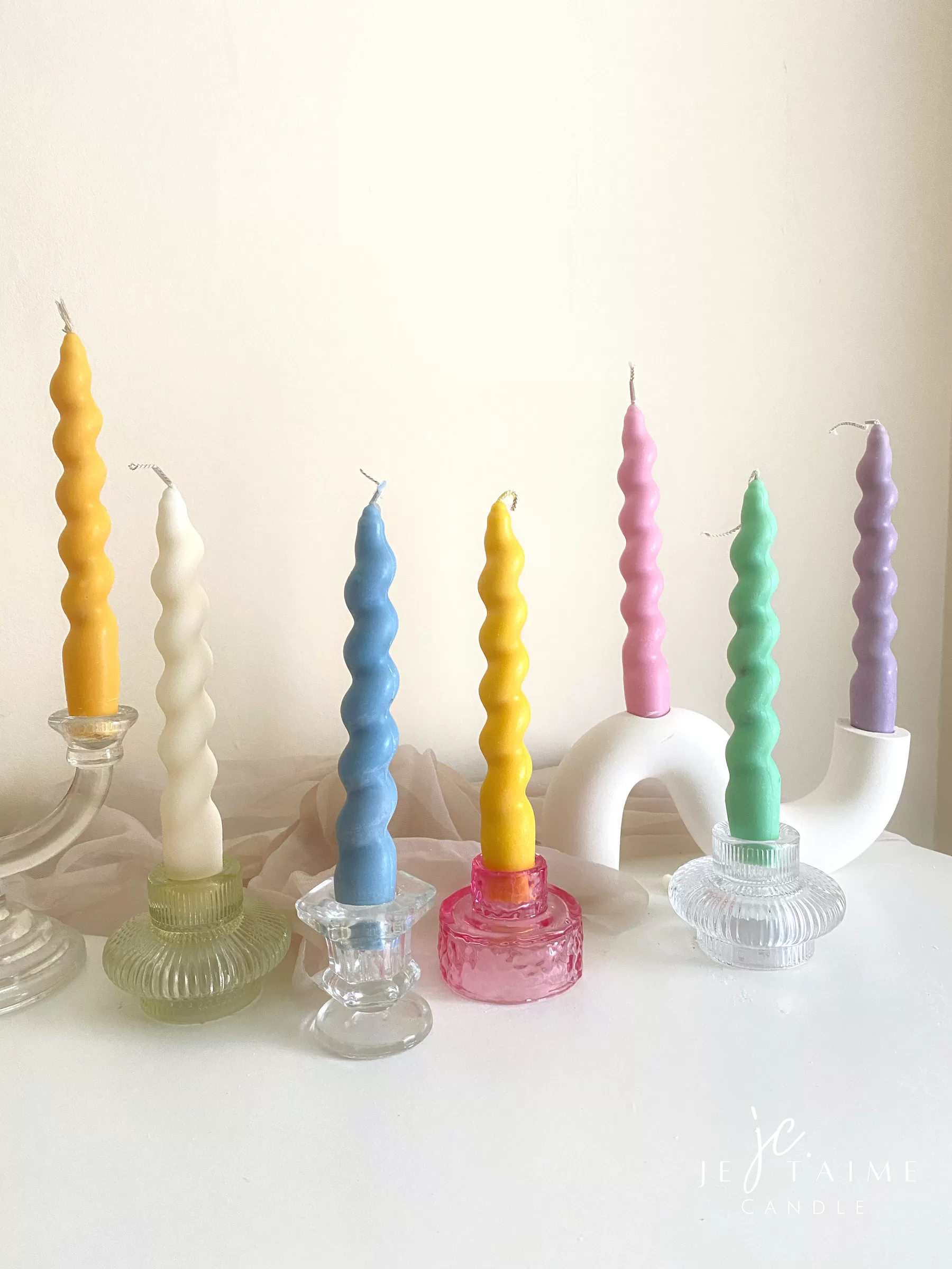 Set of colorful spiral twist soy wax taper candles in pastel green, pink, lavender, blue, yellow, and cream, displayed in clear glass holders, perfect for dinner table decor, wedding centerpieces, and modern home styling.