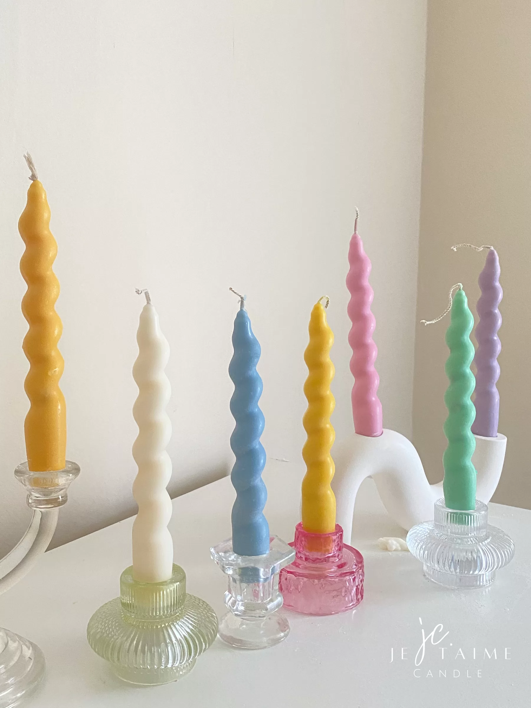 Set of colorful spiral twist soy wax taper candles in pastel green, pink, lavender, blue, yellow, and cream, displayed in clear glass holders, perfect for dinner table decor, wedding centerpieces, and modern home styling.