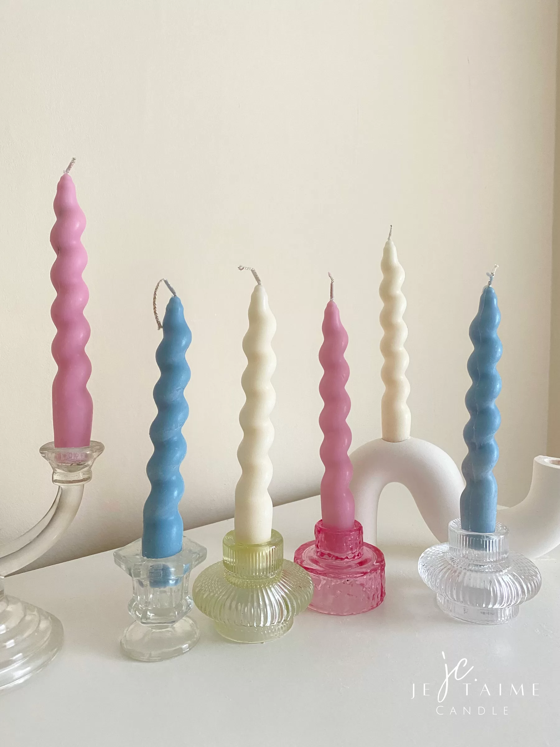 Set of colorful spiral twist soy wax taper candles in pastel pink, blue and cream, displayed in clear glass holders, perfect for dinner table decor, wedding centerpieces, and modern home styling.