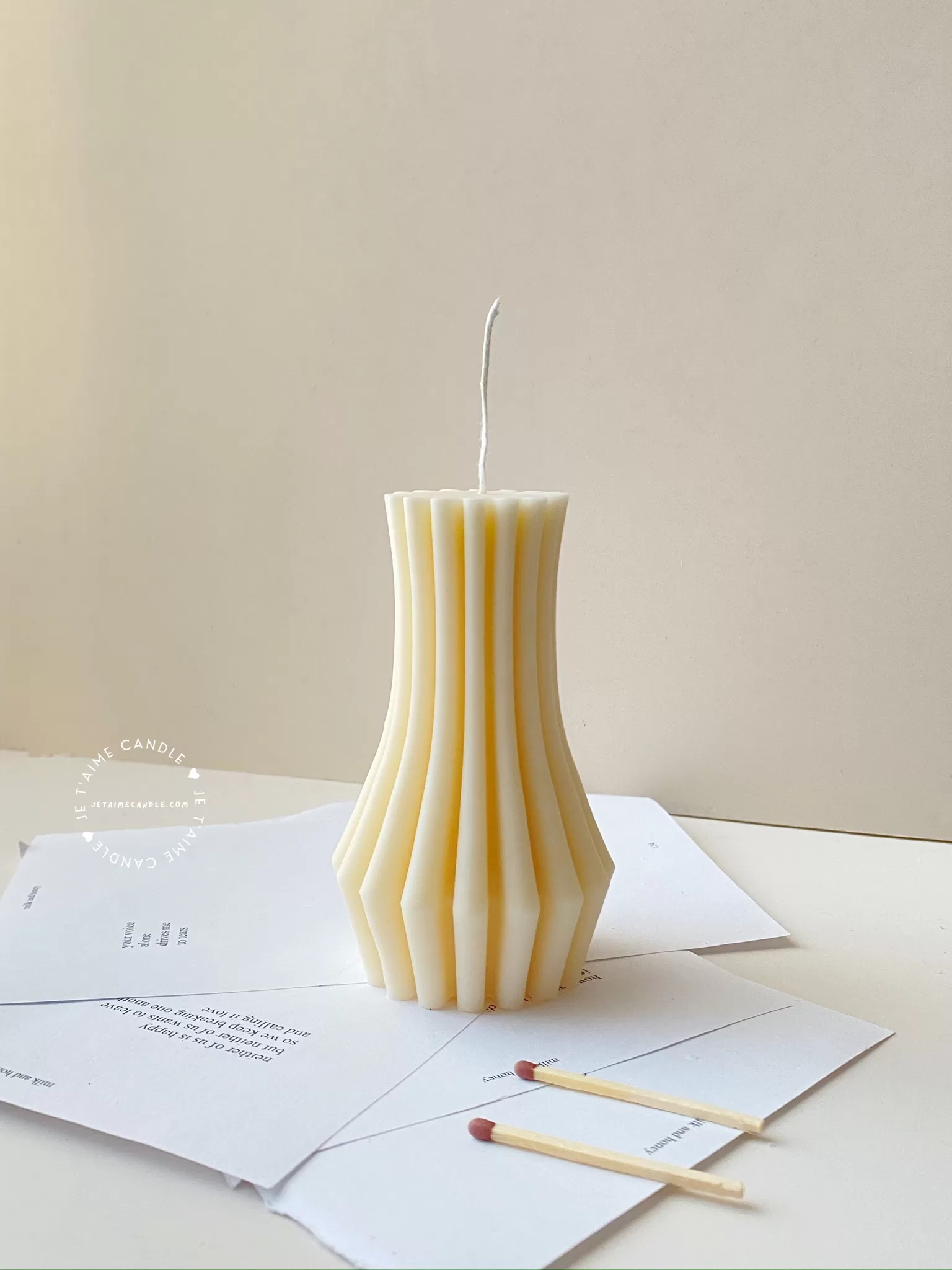 Handmade vase column aesthetic candle in ivory soy wax with a modern fluted design, displayed on a white stone base with pampas grass and other decorative candles in the background. This sculptural column candle is perfect for minimalist home décor, wedding centerpieces, or as a unique handmade gift, adding timeless elegance and modern style to any space.
