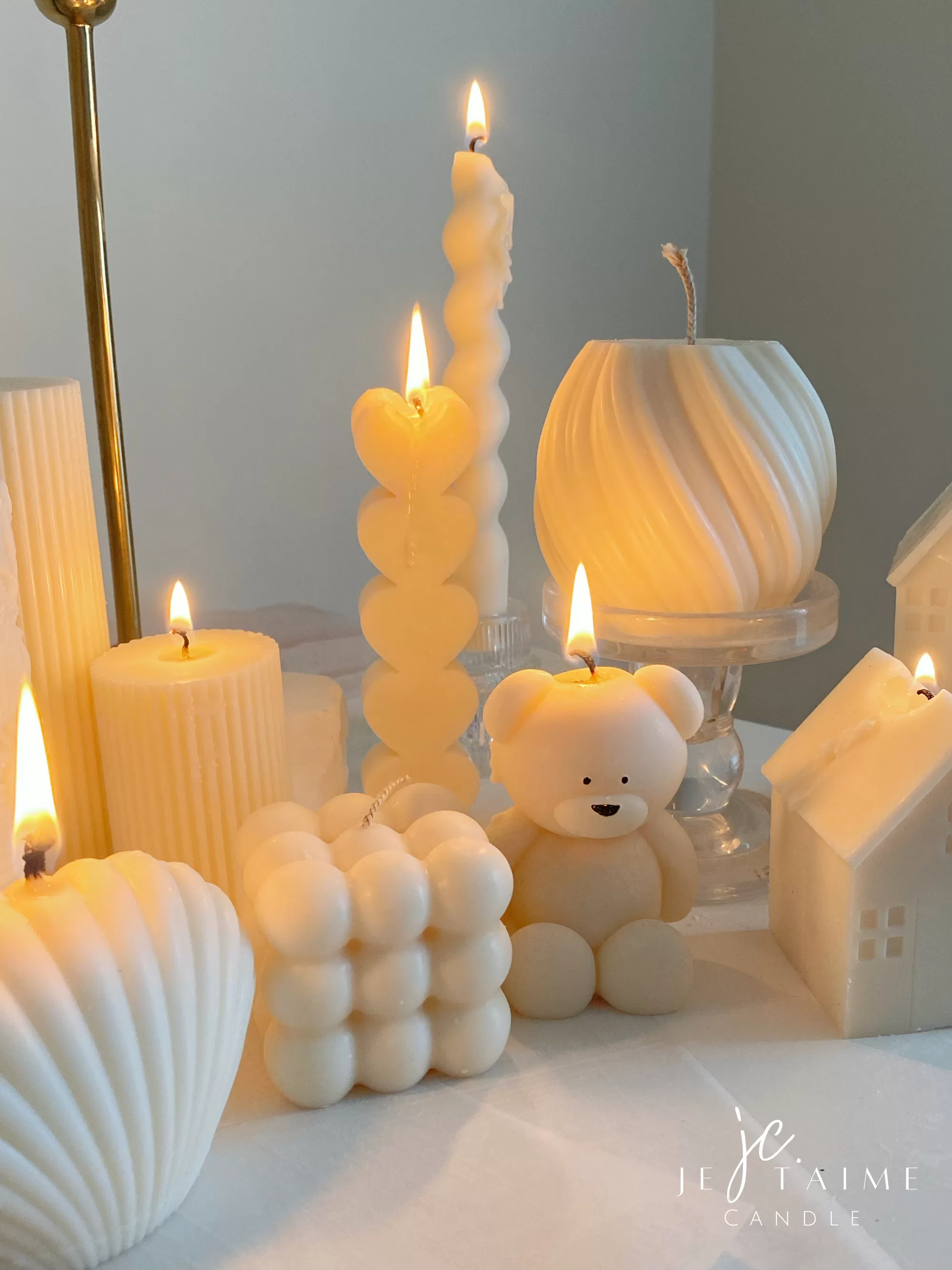Handmade soy wax decorative candles in creamy white, including ribbed pillar, bubble cube, spiral twist, heart-shaped, bear-shaped, and swirl ball designs, lit for cozy aesthetic home décor, wedding table decoration, or unique gift ideas.