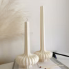 “Two lit sculptural candles with ribbed bases placed on top of a stack of design books, beside a candle snuffer and decorative pampas grass in a minimal, modern setting.