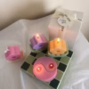 A pink yin-yang candle with two flames sits on a green and white tiled surface. A white gift box with a 